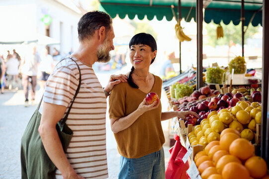 Couple Shopping at Outdoor Farmers Market &mdash; Asian Woman Holding Apple and Smiling With Partner