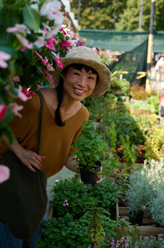 Asian Woman Smiling at Plant Market With Straw Hat Holding A Potted Herb in Outdoor Nursery