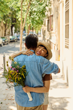 Couple Hugging on Tree-Lined City Street With Flowers &mdash; Asian Woman in Straw Hat