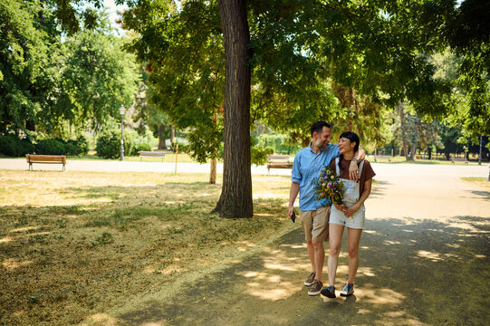 Couple Walking in Park Together With Bouquet, Smiling Asian Woman and Man Enjoying Summer Stroll