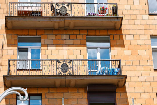 Multi story residential building facade with ornate iron balconies under natural sunlight. Car tires wrapped in protective blue plastic bags stored on an apartment balcony with wrought iron railing