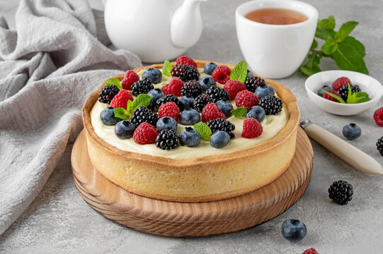 Summer tart with vanilla custard cream and fresh berries with a cup of tea on a gray concrete background. Delicious dessert.