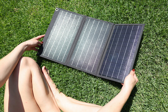 A person enjoys a sunny afternoon, sitting on lush grass while handling a portable solar panel. The warm sun energizes creativity and relaxation.