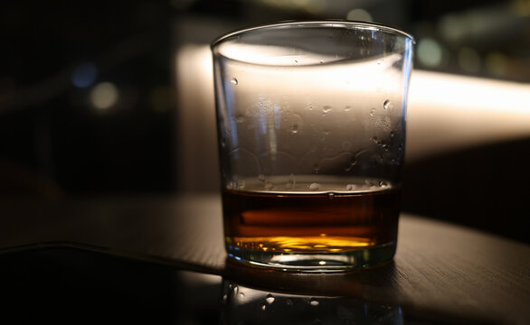 A glass of whiskey sits on a polished table, catching the soft glow of the lounge lights. The rich amber liquid sparkles, inviting relaxation and conversation in the evening.