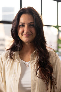Woman standing and facing camera in studio by grid windows, wearing beige shirt and pendant