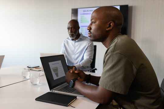 African American colleagues sitting at conference table reviewing funnel-chart on laptop, notebook