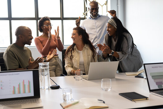 Diverse coworkers applauding central presenter using laptop at conference table in business casual