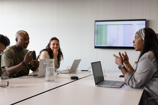 Diverse coworkers in business wear discussing spreadsheet at conference table with laptops, pitcher