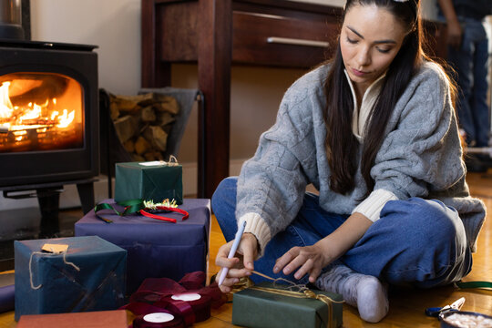 Adult woman and adult sitting on wood floor wrapping gifts with twine and pen near stove