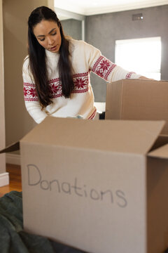 Adult woman leaning forward packing donation boxes in home with green blanket wearing white sweater