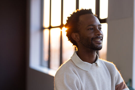 Adult man standing with arms crossed, looking right in loft by paned window wearing ribbed sweater
