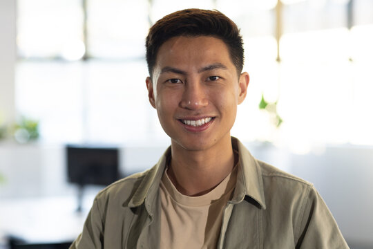 Mid-adult Asian man wearing olive overshirt smiling in office with computer monitor and plants