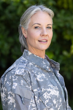 Woman in digital camouflage military jacket posing outdoors with blurred green foliage background