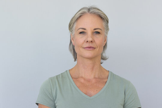 Middle-aged female posing on pale gray backdrop, wearing sage-green V-neck tee and stud earrings