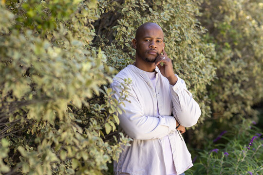 African American man standing among variegated shrubs in garden wearing button shirt and ring