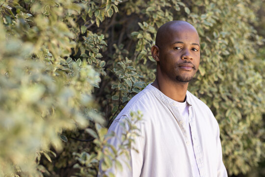 African American man standing by garden hedge wearing light shirt and white tee, copy space