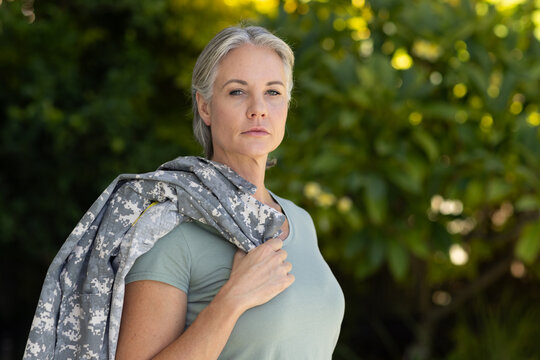 Senior woman standing in garden holding camo jacket on shoulder wearing green tee and necklace