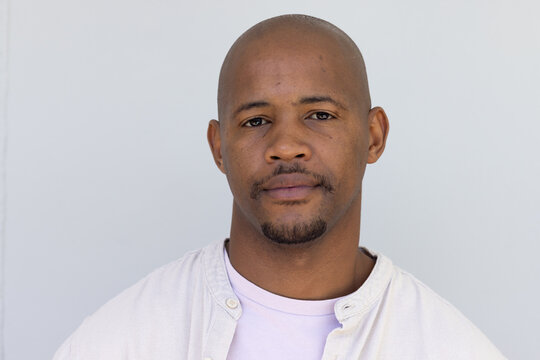 African man posing, looking into camera in gray studio wearing off-white shirt and lavender tee