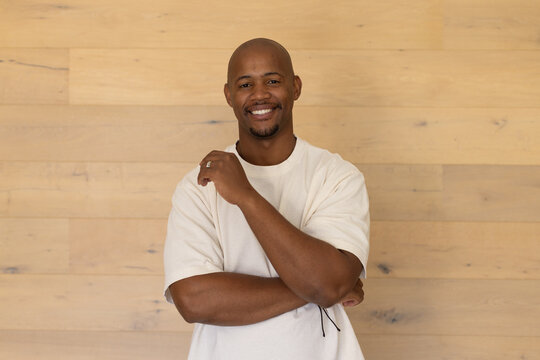 African American man standing centered on oak wall, wearing beige tee, showing ring and bracelet