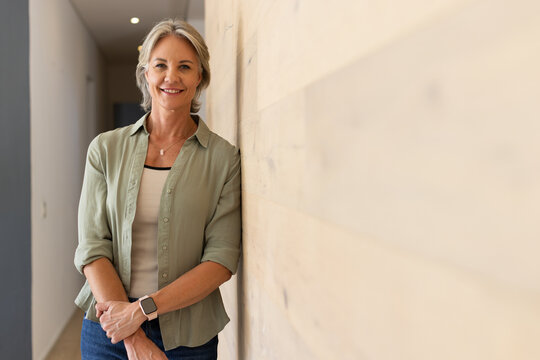 Middle-aged woman leaning against wood wall in corridor, showing smartwatch and pendant, copy space