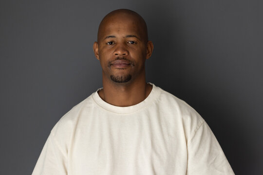 African American man posing against gray backdrop, wearing cream crewneck, in soft studio lighting