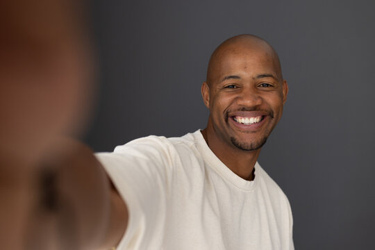 African man smiling while reaching toward smartphone in studio wearing cream shirt