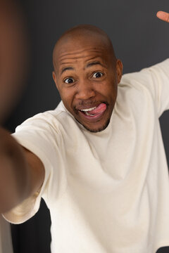 Adult man wearing white shirt making playful face, sticking tongue out holding smartphone in studio