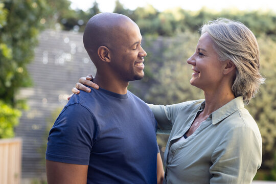 Couple standing in yard, woman touching man's shoulder, wearing green shirt and navy tee, pendant