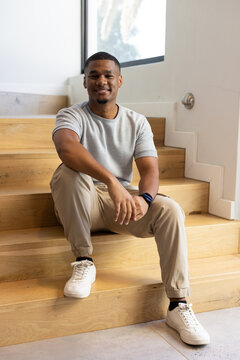 Man sitting on light-wood staircase in modern foyer, wearing white sneakers and smartwatch