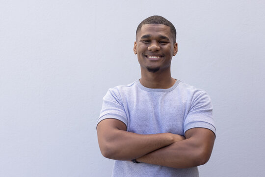African American man smiling, arms crossed against gray wall, wearing gray Tshirt, dark wristband