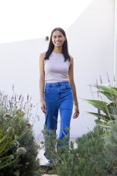 African American woman walking along paved walkway between planters and white wall wearing sneakers