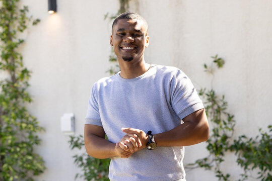 African American man standing smiling at courtyard wall wearing gray shirt watch, climbing vines