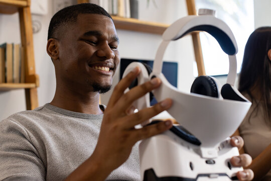 African friends sitting in living room, man handling white VR headset and adjusting straps