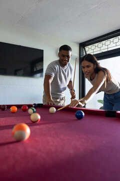 African American couple playing pool at home on red-felt table, aiming with cues and cue bridge