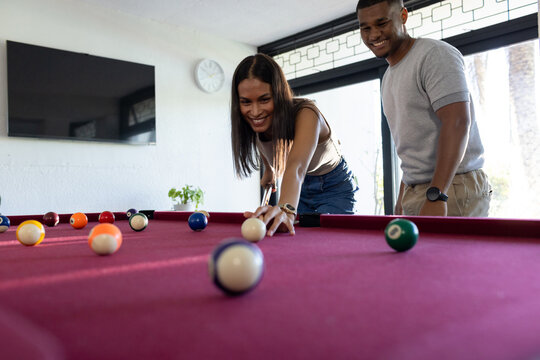 African American couple playing pool, woman leaning over burgundy-felt table lining up cue shot