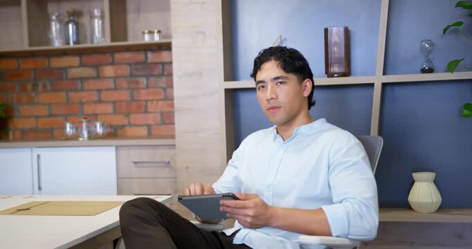 Asian adult male tapping and swiping tablet while shifting to upright at home office, smiling
