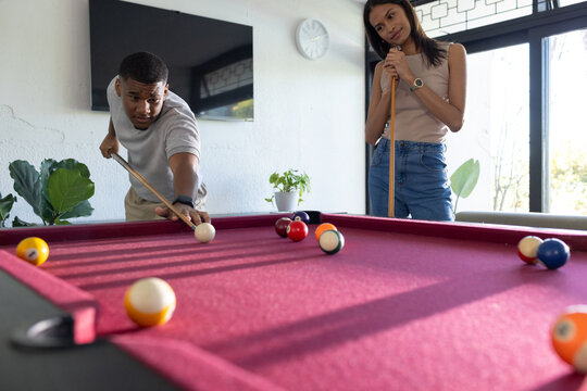 African couple playing billiards in home game room on burgundy pool table with cues