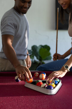 African American couple leaning over pool table at home racking balls into rack woman with cue