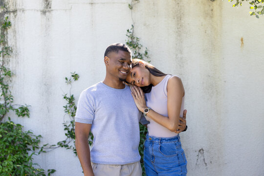 African American couple embracing at stucco wall with vines and greenery, woman in tank top, watch