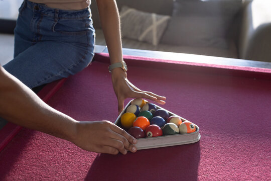 African couple arranging triangle-pool-rack on maroon-felt table, woman-in-denim-skirt, watch, sofa