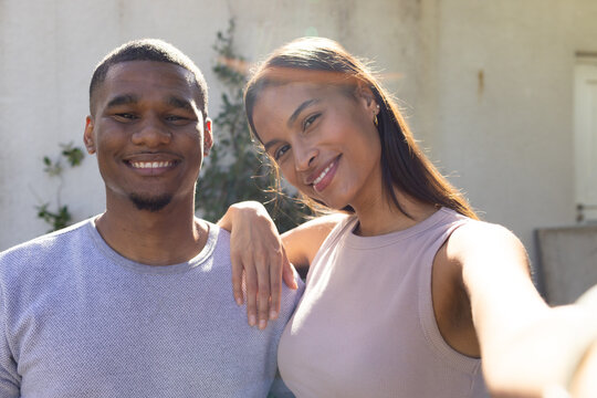 African American couple standing close on patio against stucco wall, taking selfie with smartphone