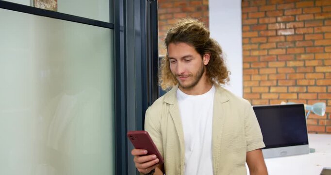 Man holding red smartphone scrolling and laughing while reading message in office corridor