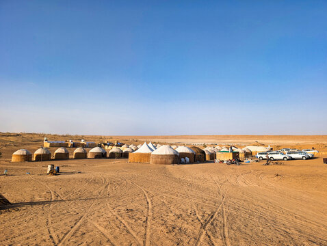 View of a traditional yurt camp set in the sandy desert landscape with parked off-road vehicles under a clear blue sky near the Darvaza Gas Crater in Derweze, Dasoguz Region, Turkmenistan.