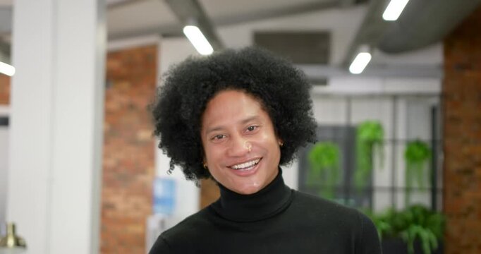 African male responding to camera, smiling, tilting head in black turtleneck at office