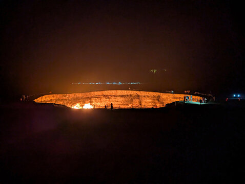 View of the glowing Darvaza Gas Crater at night with silhouettes of people standing on the rim in the Karakum Desert, Derweze, Dasoguz Region, Turkmenistan.