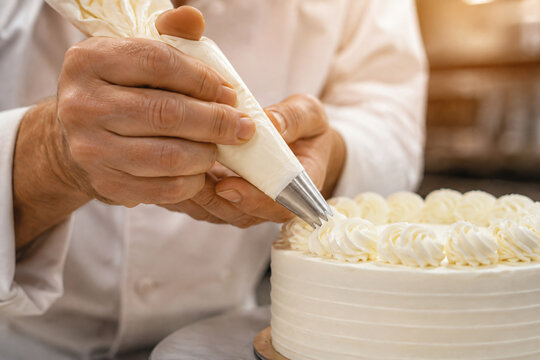 Pastry chef decorating a white cake with piped buttercream frosting using a professional piping bag