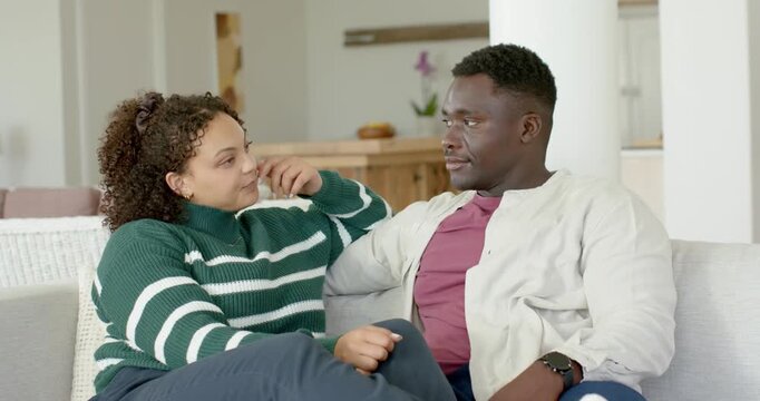 African American couple sitting on light sofa, woman starting talk seeking comfort, dabbing tissue