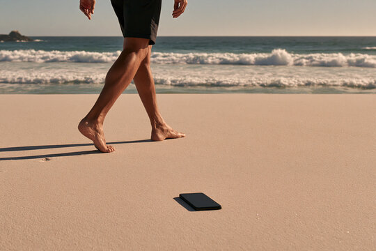 A person walks barefoot along a pristine sandy beach leaving a black smartphone behind capturing a moment of solitude by the crashing ocean waves