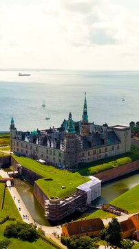 Vertical video. Helsingor, Denmark. Kronborg Castle, a Renaissance fortress with sandstone walls and copper spires, Drone footage over the Oresund Strait under bright summer sky. Drone footage, Depar