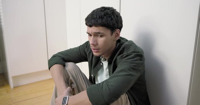 African American man sitting on hardwood floor, reacting to white smartwatch buzzing and reflecting